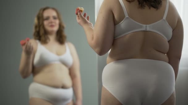 Избыточный вес молодая женщина стресс едят перед зеркалом, ненавидя ее жирное тело — стоковое видео