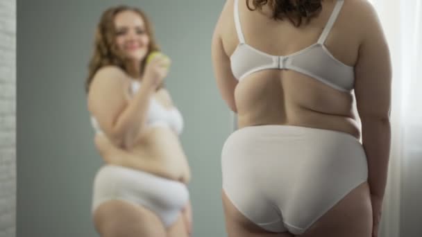 Plus size lady äta äpple framför spegel, njuter resultaten av hälsosam kost — Stockvideo