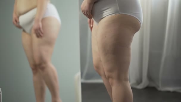 Kvinna som tittar i spegeln, celluliter och bristningar på höfter, röra stor mage — Stockvideo