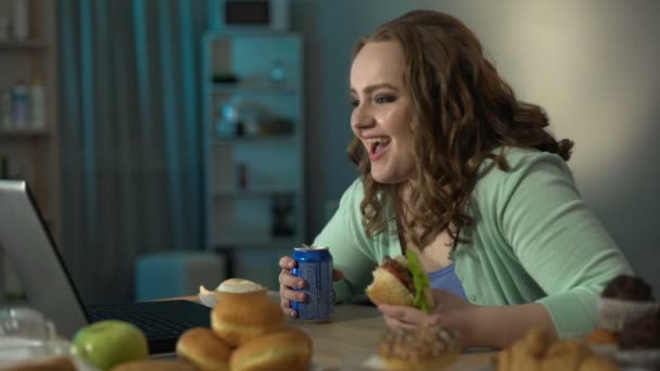 Adolescente chica disfrutando de la comedia en portátil beber refrescos y comer hamburguesa mientras tanto — Vídeo de stock