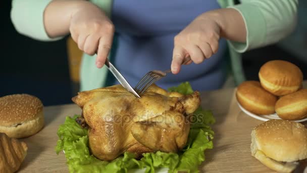 Donna grassa intagliare approssimativamente pollo arrosto con forchetta e coltello, mangiare cibo spazzatura — Video Stock