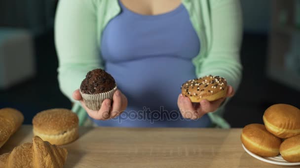 Femme tenant muffin et beignet, beaucoup de pâtisserie sur la table, trop manger de bonbons — Video