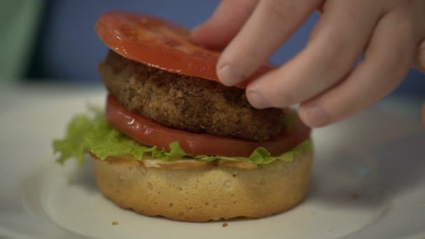 Ребенок укладывает ингредиенты бургеров, готовится к употреблению нездоровой пищи, проблемы ожирения — стоковое видео