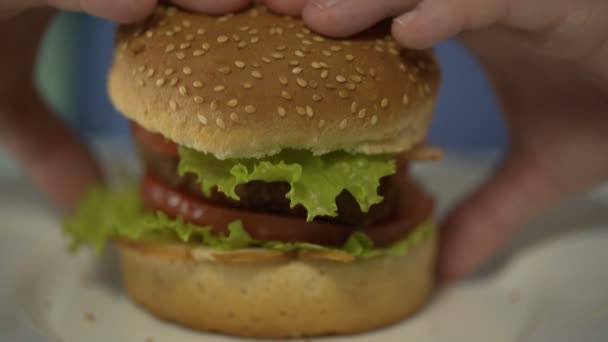 Женщина-подросток кусает большой бургер, проблемы с перееданием фаст-фуда, руки крупным планом — стоковое видео