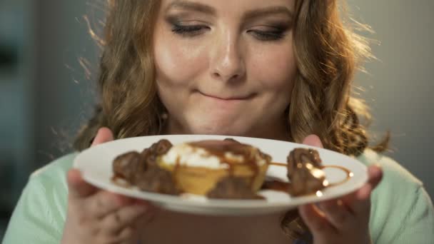 Подросток с голодными глазами, любующийся тарелкой, полной сладостей под шоколадным соусом — стоковое видео