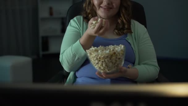 Девушка наслаждается глупой программой по телевизору дома, ест и разбрасывает попкорн вокруг — стоковое видео