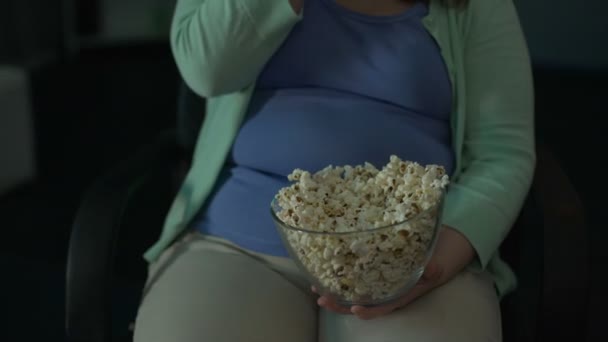 Mujer gorda tomando un puñado de palomitas de maíz de un tazón y comiendo mientras ve una película — Vídeos de Stock