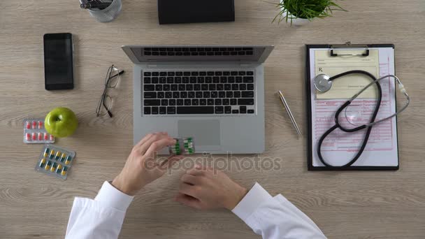 Médico tomando pastillas y escribiendo información en el ordenador portátil, haciendo la prescripción — Vídeo de stock