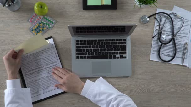 Arzt schaut sich Versicherung des Patienten an und tippt Informationen auf Laptop — Stockvideo