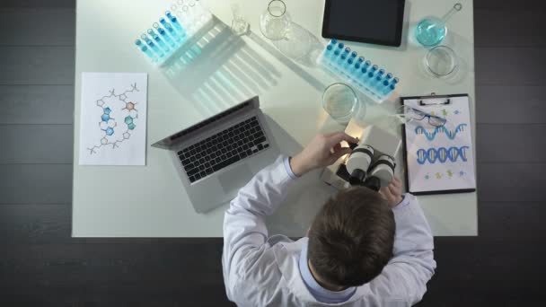 Trabajador de laboratorio mirando al microscopio, registrando el descubrimiento científico en el portátil — Vídeos de Stock