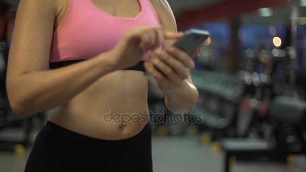 Young female scrolling on mobile phone in gym, setting up training application — Stock Video
