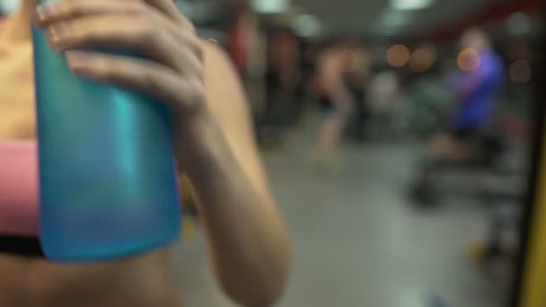 Deportiva mujer bebiendo agua después de terminar los ejercicios en el gimnasio, primer plano de la botella — Vídeo de stock