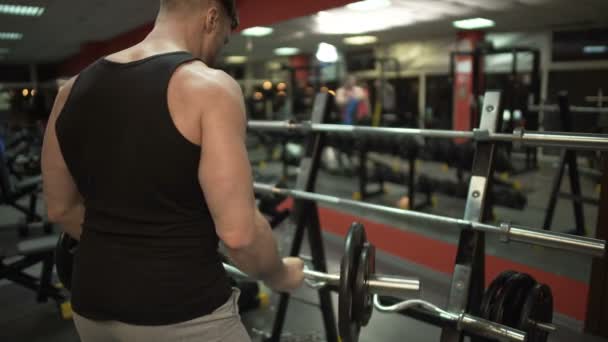 Sportowy facet robi kilka lift-ups z curl bar, wprowadzenie go z powrotem na stoisku w siłowni — Wideo stockowe