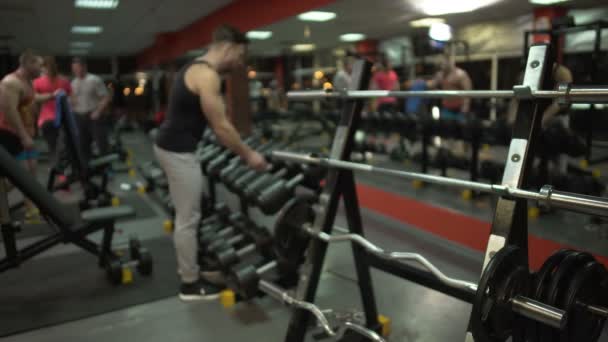 Здоровый парень приближается к гантели стенд и принимать большие фиксированные веса, чтобы сделать упражнения — стоковое видео