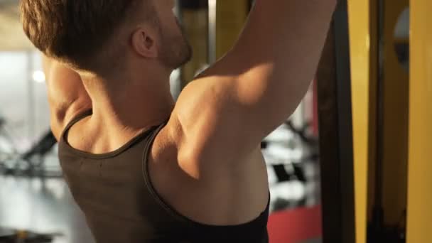 Hunky man doen van pull-down oefening in de gym met zonlicht valt op zijn rug — Stockvideo