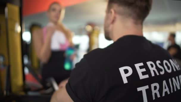 Jovem flertando com personal trainer após o treino, casal conversando no ginásio — Vídeo de Stock