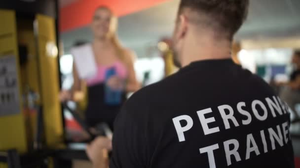 Тренер мужского пола разговаривает с коллегой в спортзале, пара знакомится — стоковое видео