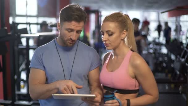 Trainer und seine attraktive Kundin diskutieren Trainingsprogramm im Fitnessstudio — Stockvideo