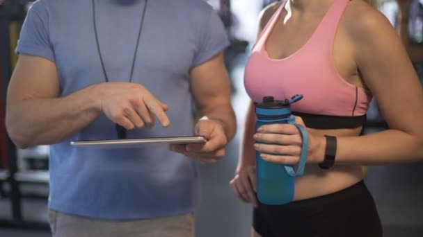 Προπονητής εξηγεί το χρονοδιάγραμμα κατάρτισης σε θηλυκό πελάτη, χρησιμοποιώντας το tablet στο γυμναστήριο — Αρχείο Βίντεο