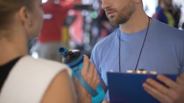 Jonge vrouw communiceren met trainer in de sportschool, het drinken van water na training — Stockvideo