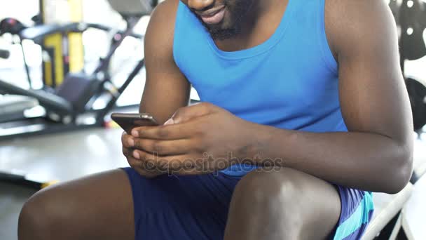 Homem afro-americano satisfeito vestindo roupas esportivas navegando em smartphones no ginásio — Vídeo de Stock