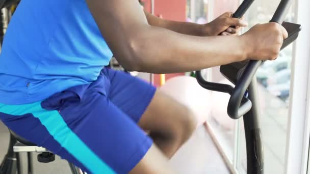 Homem afro-americano propositado montando uma bicicleta de exercício no clube de fitness, esporte — Vídeo de Stock
