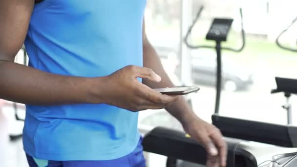 Sportsman andando na esteira rolante e usando o aplicativo de fitness em seu smartphone — Vídeo de Stock