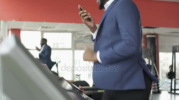 Treinamento masculino afro-americano sério em esteira rolante e conversando no telefone celular — Vídeo de Stock