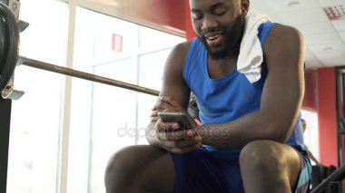 Gülümseyen Afro-Amerikan adam spor salonunda oturuyor ve Smartphone'da görüntülü arama yapma