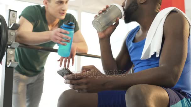 Два спортивных друга пьют воду и говорят о соревнованиях в спортзале — стоковое видео
