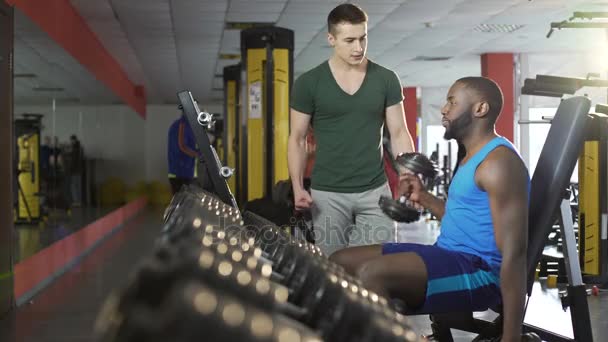 Joven amigo motivador de apoyo durante el entrenamiento de mancuerna en el gimnasio, fitness — Vídeo de stock