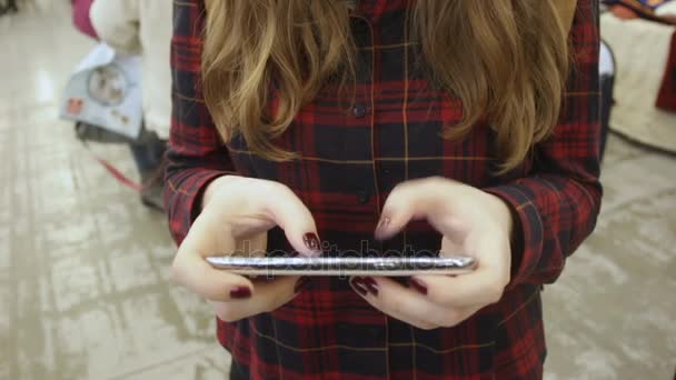 Девушка печатает сообщение на своем гаджете, используя мобильное приложение в торговом центре — стоковое видео