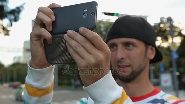 Hombre divertido en la tapa de la filmación de vídeo en el teléfono inteligente en la calle, ropa moderna — Vídeo de stock