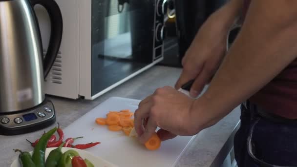 Мужчина аккуратно вырезает морковь, чтобы приготовить вкусный ужин для своей девушки — стоковое видео
