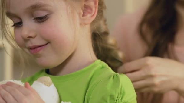 Любляча мати плете волосся дочки і цілує свою дитину, сім'ю і догляд — стокове відео