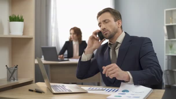 Empleado masculino terminando hablar por teléfono móvil, trabajando en el ordenador portátil, satisfecho — Vídeos de Stock