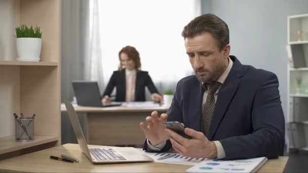 Homem de terno verificando celular, digitando dados no laptop, trabalho de escritório, distração — Vídeo de Stock