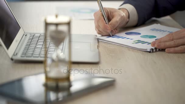 Worker marking diagrams on paper, hourglass trickling, approach of deadline — Stock Video