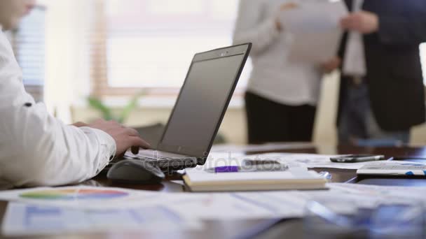 Lavoratore prendere appunti sul computer portatile mentre due colleghi discutono documenti, ufficio — Video Stock