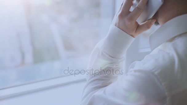 Successful young man standing in front of window, having conversation over phone — Stock Video