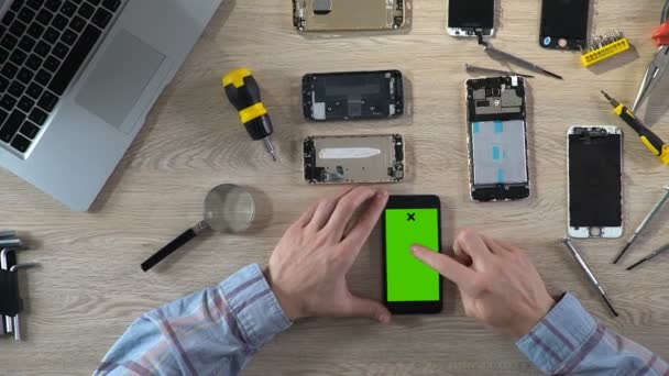 Mãos de técnico rolando no smartphone com tela verde, diagnósticos — Vídeo de Stock