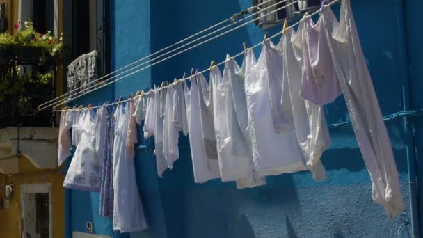 Чистий одяг, що мерехтить у вітрі, висить на яскраво-синьому фасаді будинку — стокове відео