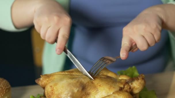 Gorda hembra cortando pollo asado áspero con cubiertos, nutrición poco saludable — Vídeos de Stock