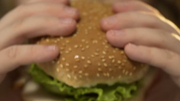 Девочка с избыточным весом кусает большой бургер и жует его, фаст-фуд — стоковое видео