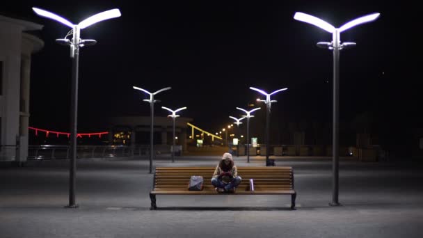 Happy girl having fun with mobile app on gadget, sitting on bench in night city — Stock Video