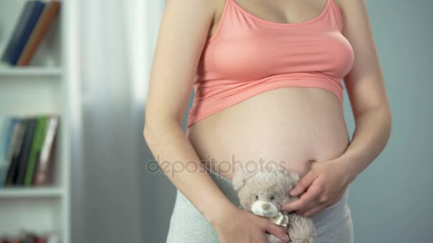 Mujer soñadora con vientre embarazada abrazando juguete oso tiernamente, madre sustituta — Vídeos de Stock