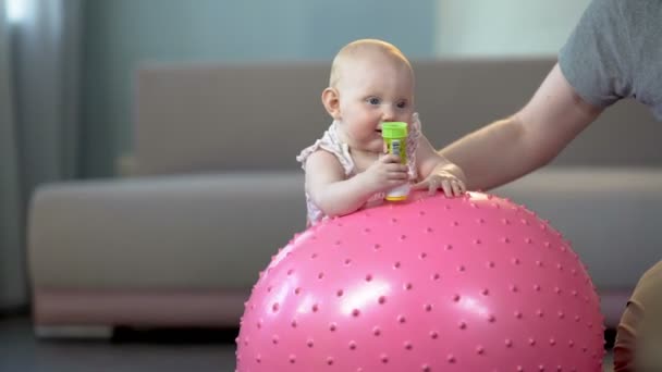 Симпатичный здоровый ребенок с удовольствием прыгает на большом мяче, занимается фитнесом для младенцев — стоковое видео
