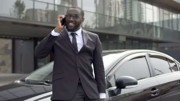 Afro-americano coqueteando con una chica en el teléfono, de pie cerca de su coche de lujo — Vídeos de Stock