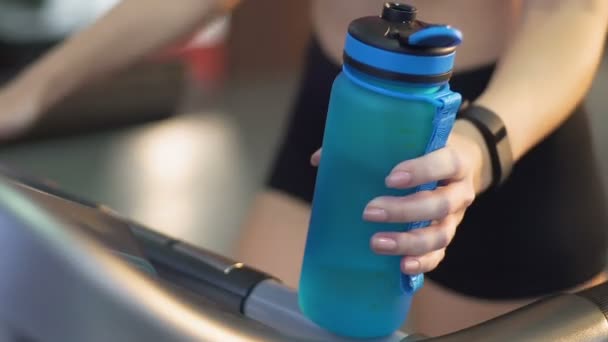 Junge Frau läuft im Fitnessstudio auf Laufband, Wasserflasche in der Hand, Wasserhaushalt — Stockvideo