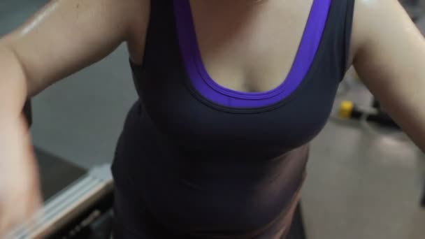 Спітніла дівчина з надмірною вагою, що ходить по біговій доріжці, тримає груди, проблеми зі здоров'ям — стокове відео